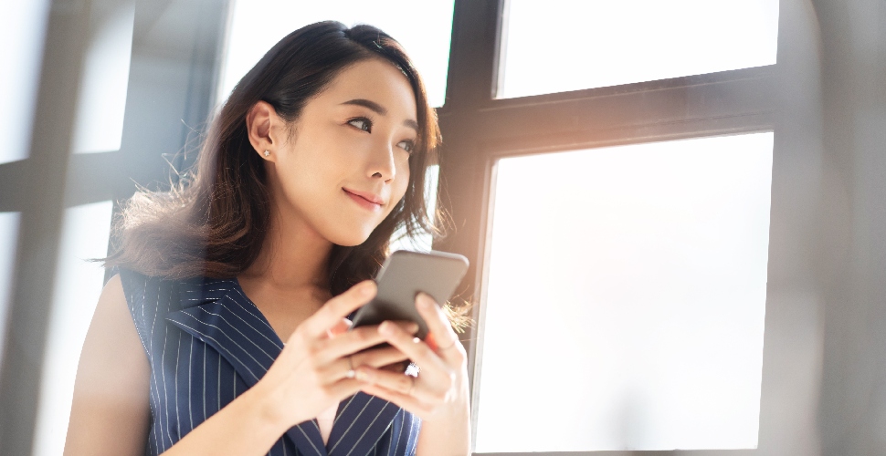 A woman holding a mobile phone and looking out the window.