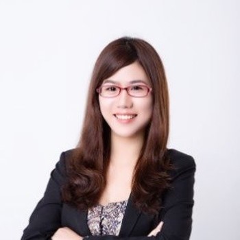 Person smiling, wearing glasses and a suit jacket, with crossed arms.