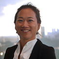 A person smiling outdoors with a cityscape in the background.