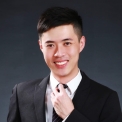 A person smiling in a suit with a dark background.