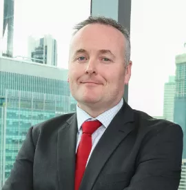 A person in a suit smiling in front of a cityscape.
