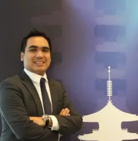 Person in a suit smiling in front of a blue background with a stylized tower design.