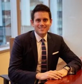 Person in suit smiling at a desk in an office.