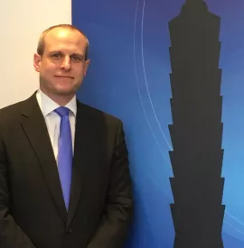 A person in a suit and tie stands next to a silhouette of a building.