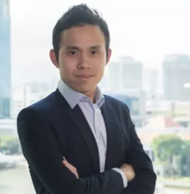 Person in a suit standing by an office window with a city view