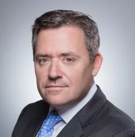 Close-up portrait of a person in a suit with a light gray background.