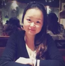 A person smiling while seated in a restaurant with others in the background.