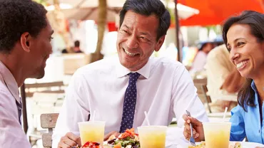三人坐在戶外餐廳的桌前微笑交流。