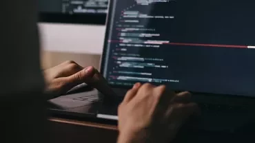 Hands typing code on a laptop in a dark room