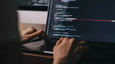Hands typing code on a laptop in a dark room