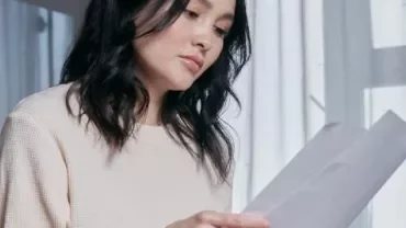 A person reviewing papers with light coming through curtains.