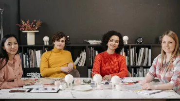 A group of people smiling at a conference table, with a bookshelf in the background.