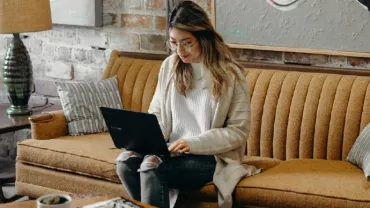 Person sitting on a vintage sofa using a laptop in a cozy room.
