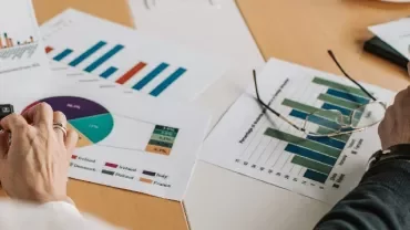Hands analyzing graphs and charts on paper with a calculator