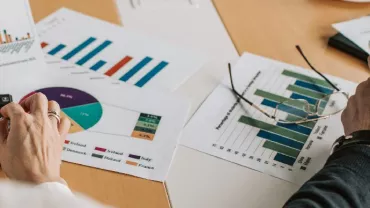Hands analyzing graphs and charts on paper with a calculator