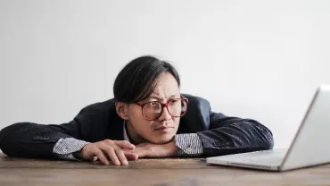 A person leaning on a desk, looking at a laptop.
