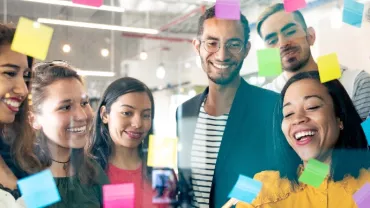 Group of people looking at sticky notes on a glass board