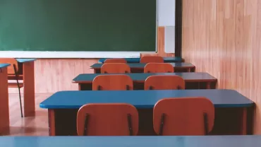 An empty classroom with arranged desks and a green chalkboard