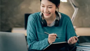An adult using a laptop and notebook at a desk.