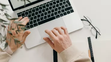 Person typing on a laptop with glasses and notebook nearby