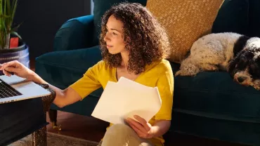 Person working on a laptop with a dog resting on the couch.