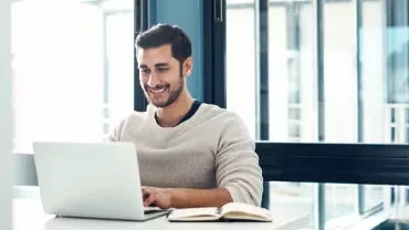 A person smiling while looking at a laptop on a table.