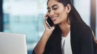 Person smiling while talking on phone and using laptop.