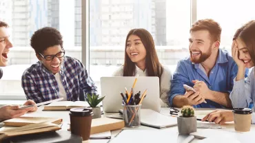 Group of students laughing and working together around a table.