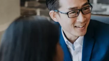 Person in a suit smiling and talking with a colleague.
