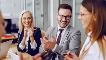 Colleagues having a cheerful discussion and clapping in a meeting.