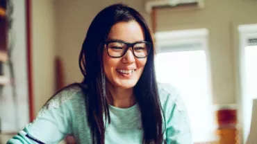 Person smiling while using a computer in a room with bookshelves.