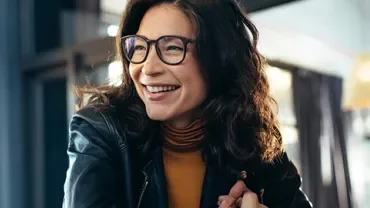 A person wearing glasses smiling while seated in a cafe.