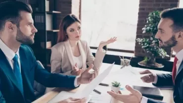 Three business professionals engaged in discussion while seated at a table