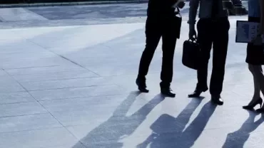 Three business professionals standing together in front of a modern office building, engaged in conversation.
