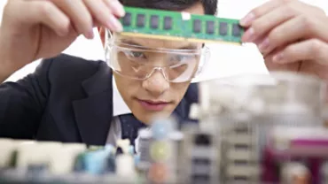 A person wearing safety goggles inspecting a computer RAM module.