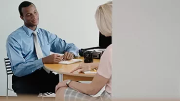 Two people having a meeting in an office, one in a blue shirt, the other in pink.