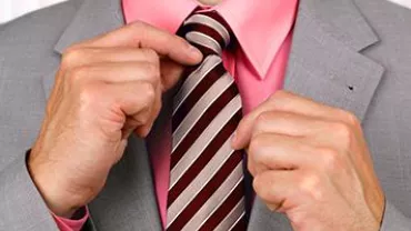 A person adjusting a striped tie, wearing a pink shirt and gray suit.