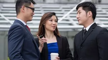 Three people having a conversation outside in business attire.