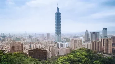 City skyline with tall buildings, lush greenery in the foreground.
