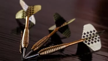 Three darts lying on a table, blurred background.