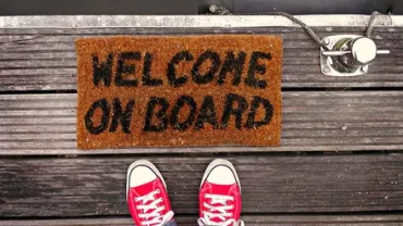 Red shoes on a wooden dock next to a welcome mat and boat rope.