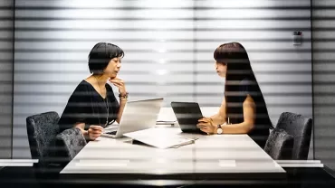 Two people sitting at a conference table using laptops.