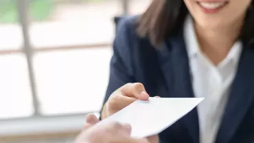 Person in a suit handing over a piece of paper.