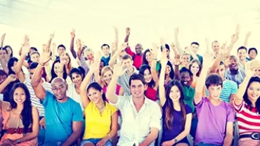 A large group smiles and waves in a bright, airy room