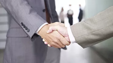 兩名商務人士握手，背景模糊多位站立人員。