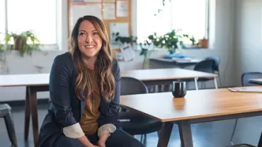 Person smiling while sitting at a desk in an office with plants.