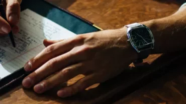 A hand wearing a watch writing on a notepad.