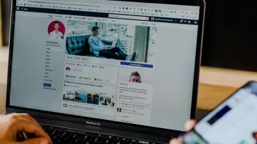 Laptop open to a social media profile next to a hand holding a smartphone.