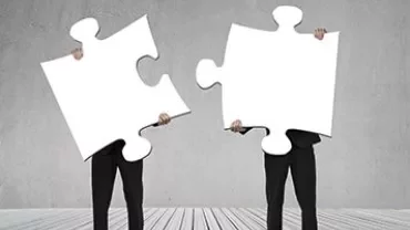 Two people holding large puzzle pieces standing on a wooden floor