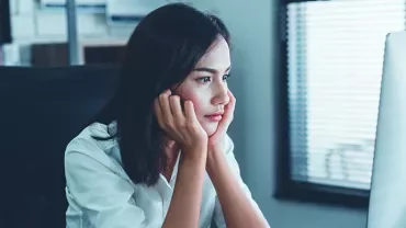 Person sitting at a desk looking thoughtfully at a computer screen.